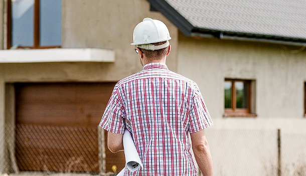 Man with white helmet and paper in front of the house